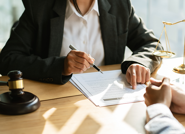 Two people sit at a desk reviewing a document; one person points at the paper with a pen. Symbols of law—a gavel and scales of justice—rest on the table, highlighting their commitment to fairness and due process.