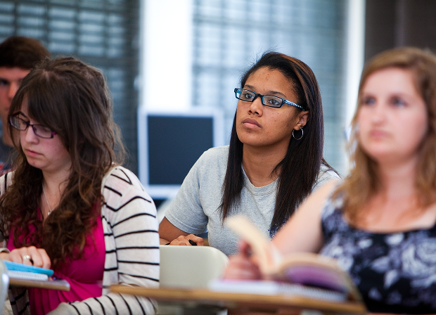 Students sit at desks in a classroom, attentively listening and taking notes about law and justice, with books and notebooks open in front of them.