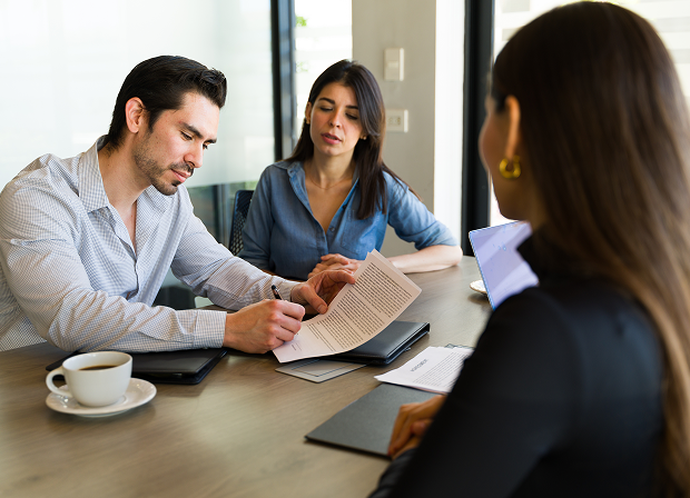 Three people are seated at a table in an office, discussing and reviewing a document about law, with a laptop and coffee cup on the table.