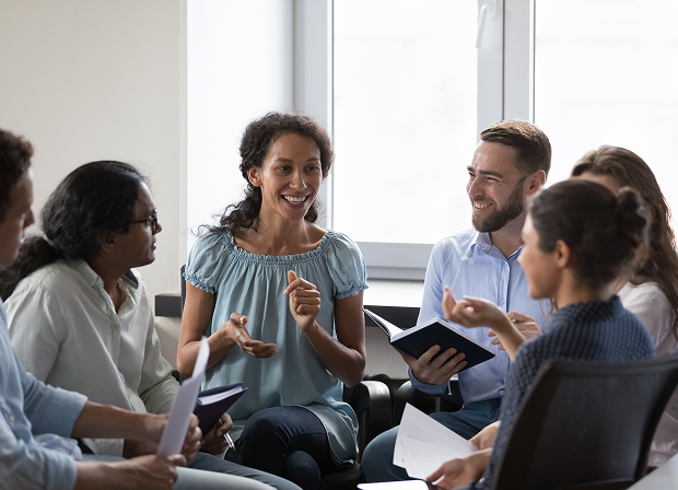 Six people sit in a circle indoors, actively engaged in a group discussion about law and justice. Some are holding notebooks, and one woman is speaking while others listen and smile.